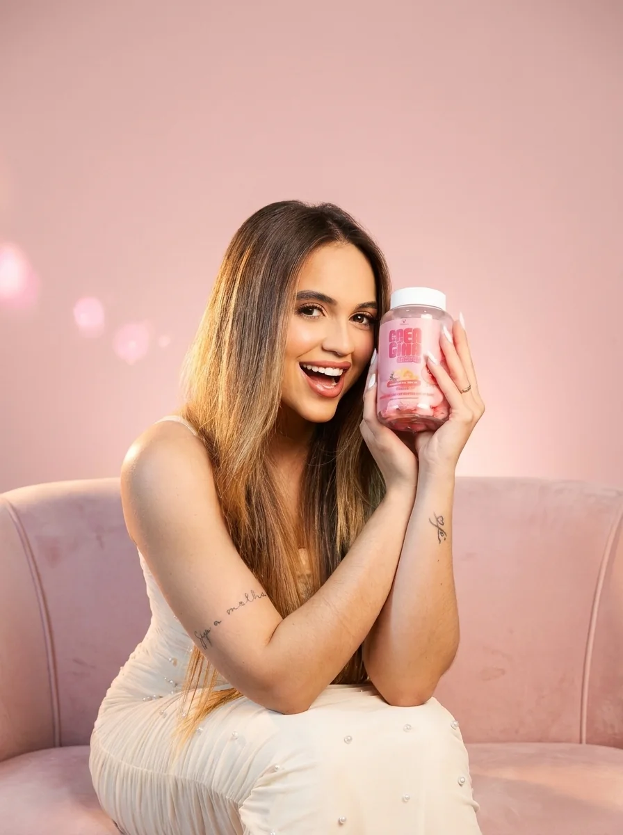 Creator sorrindo no sofá rosa com o pote de Crea Gummy junto ao rosto