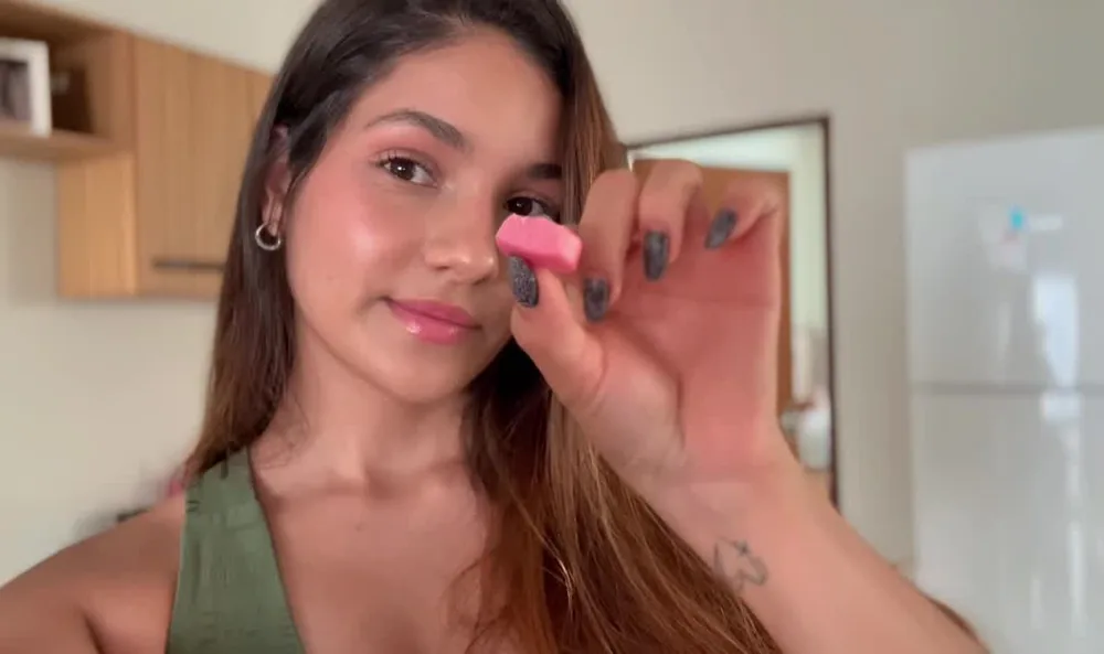 Mão segurando uma goma de Crea Gummy em formato de coração ao lado do pote aberto